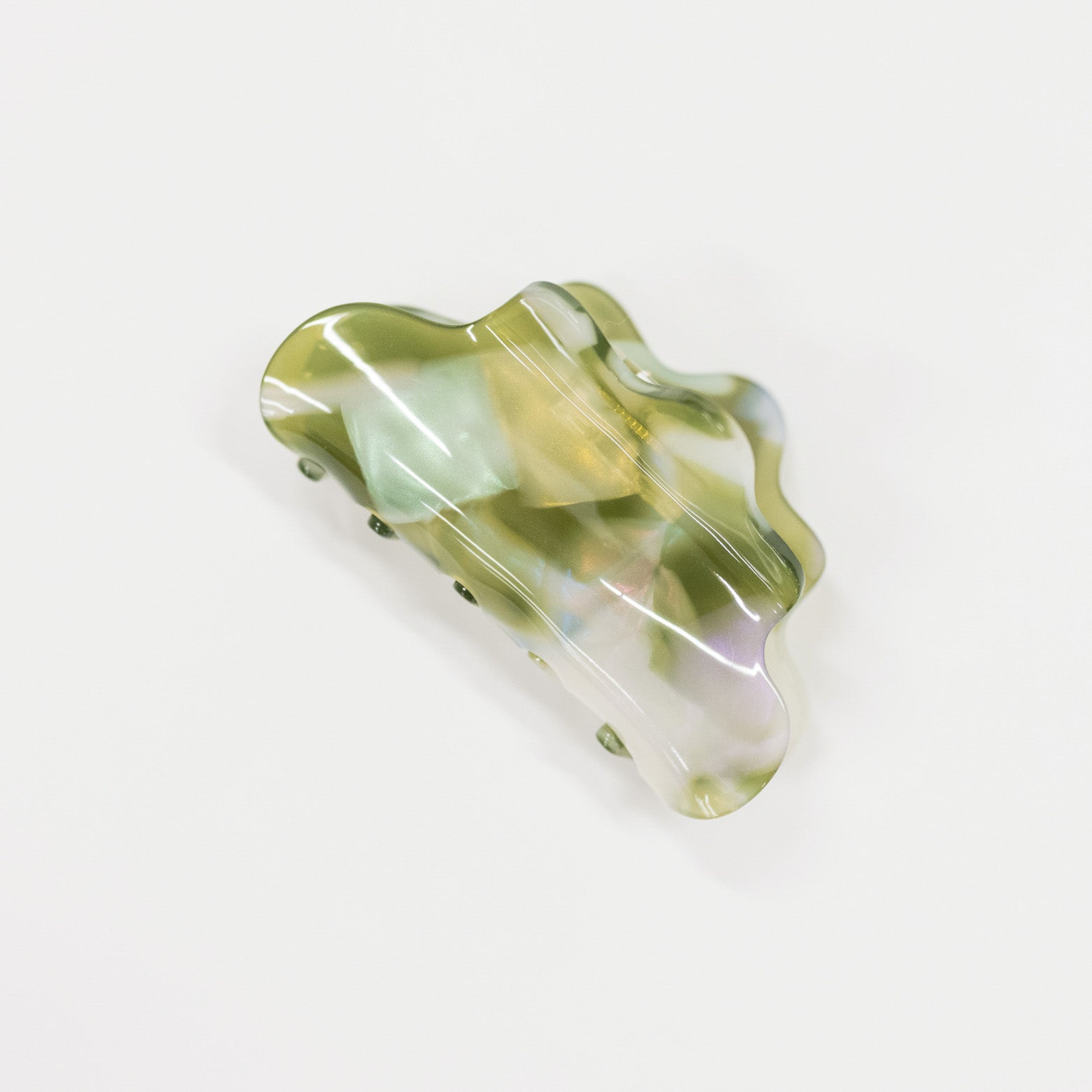 A wavy, organic-shaped hair claw clip made of iridescent resin with a mix of olive green, pale yellow, and pearlescent white tones, shown on a plain white background.