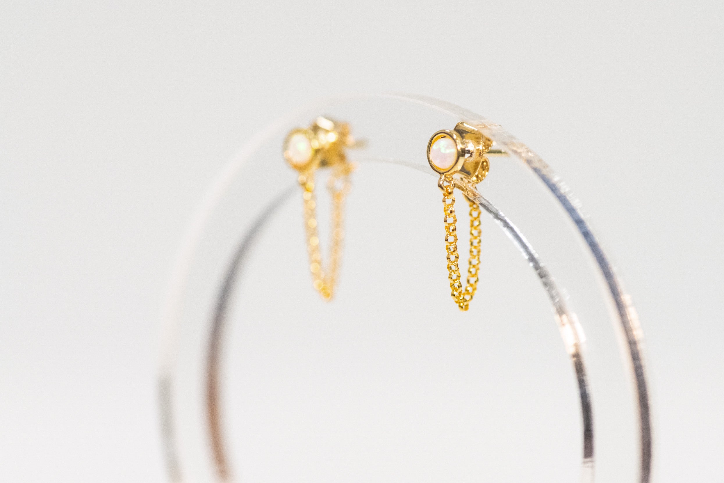 Gold hoop earrings with chain details on a light gray background