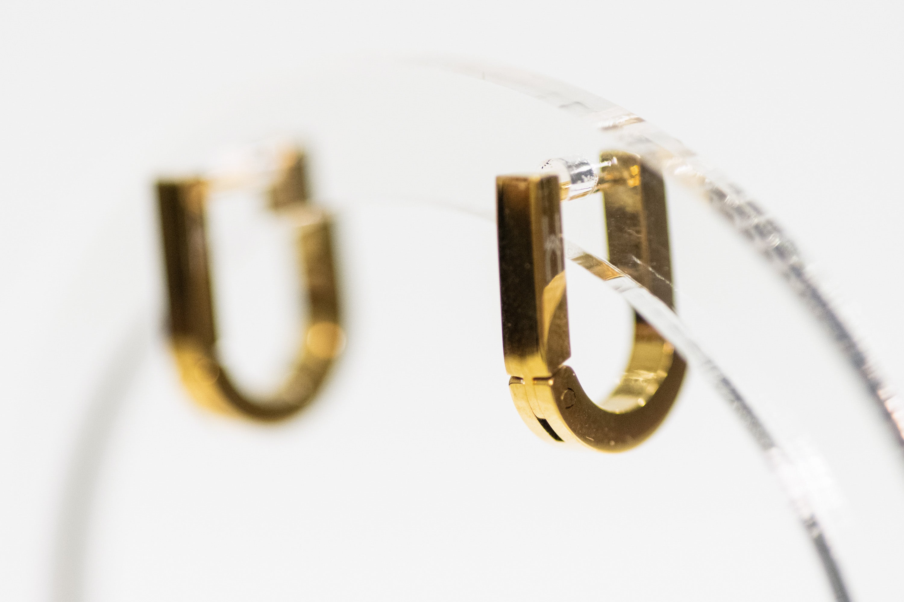 Gold hoop earrings on a clear stand with a blurred background