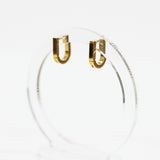 Square gold hoop earrings on a clear stand against a white background