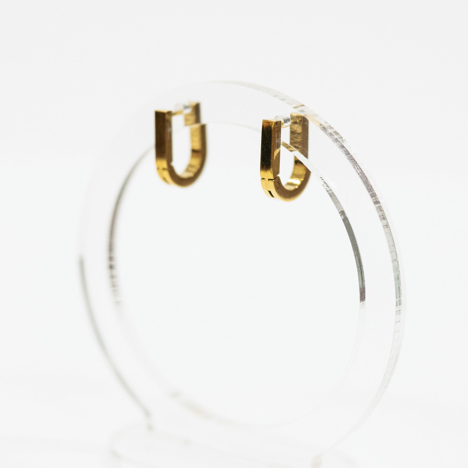 Square gold hoop earrings on a clear stand against a white background