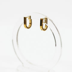 Square gold hoop earrings on a clear stand against a white background