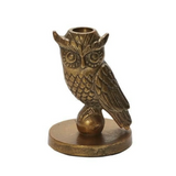 An antique bronze owl figurine perched on a small round base, designed as a candle holder with a circular cup on its head, set against a plain white background.
