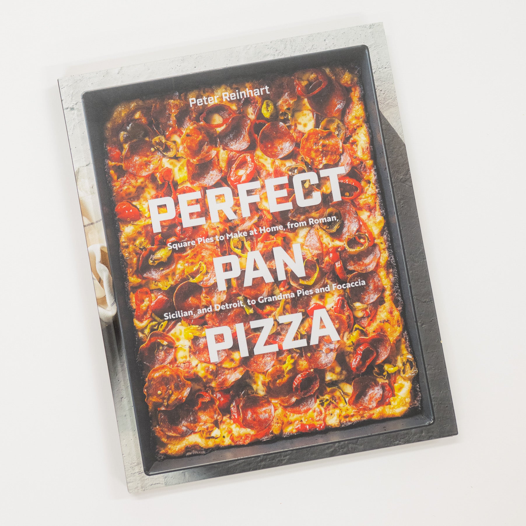 Cookbook titled 'Perfect Pan Pizza' by Peter Reinhart on a white background