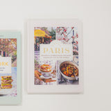 Cookbook titled 'Paris' with images of food and city scenes on a white surface.