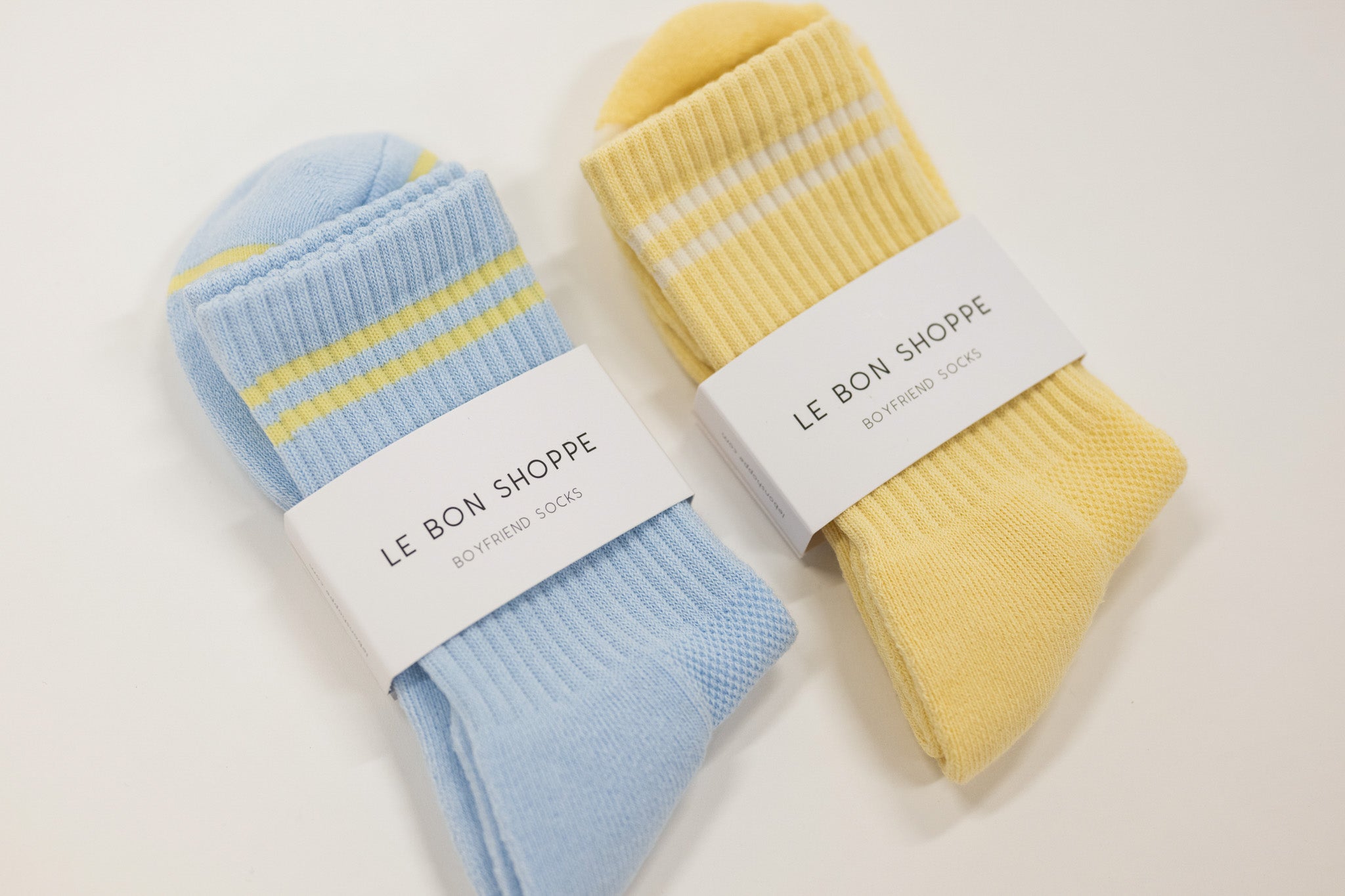 Two pairs of socks, one blue and one yellow, with 'Le Bon Shoppe' labels on a light background.
