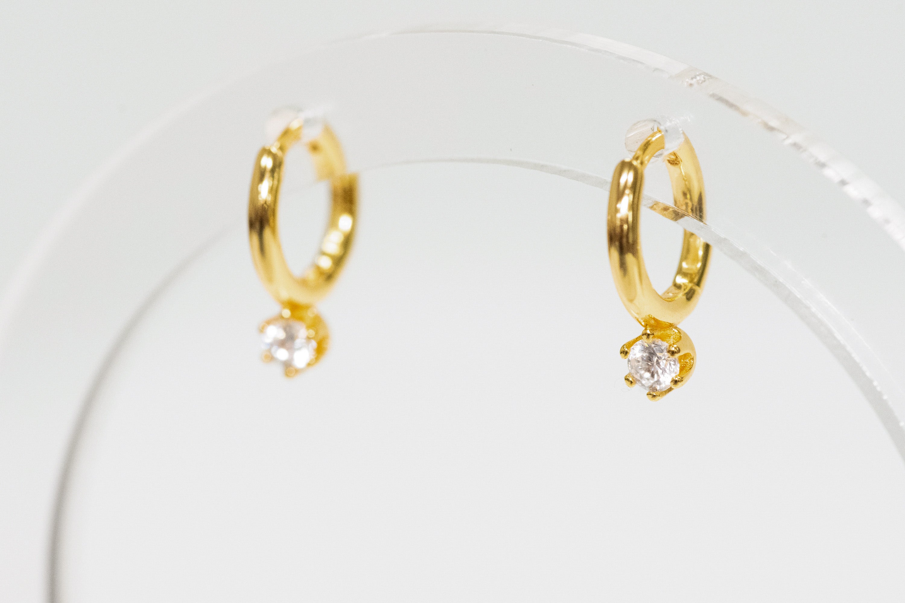 Gold hoop earrings with small CZ stud on a clear stand.