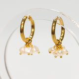 Gold hoop earrings with pearl drops on a clear stand against a white background