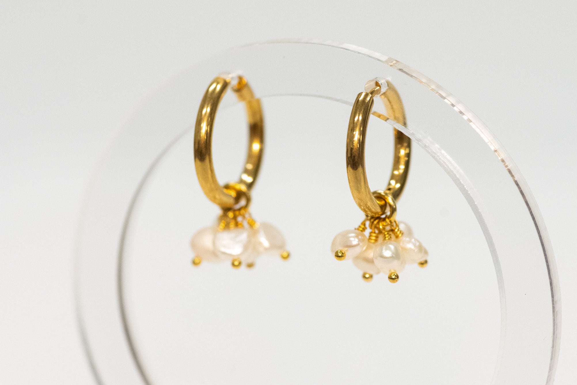 Gold hoop earrings with pearl drops on a clear stand against a white background