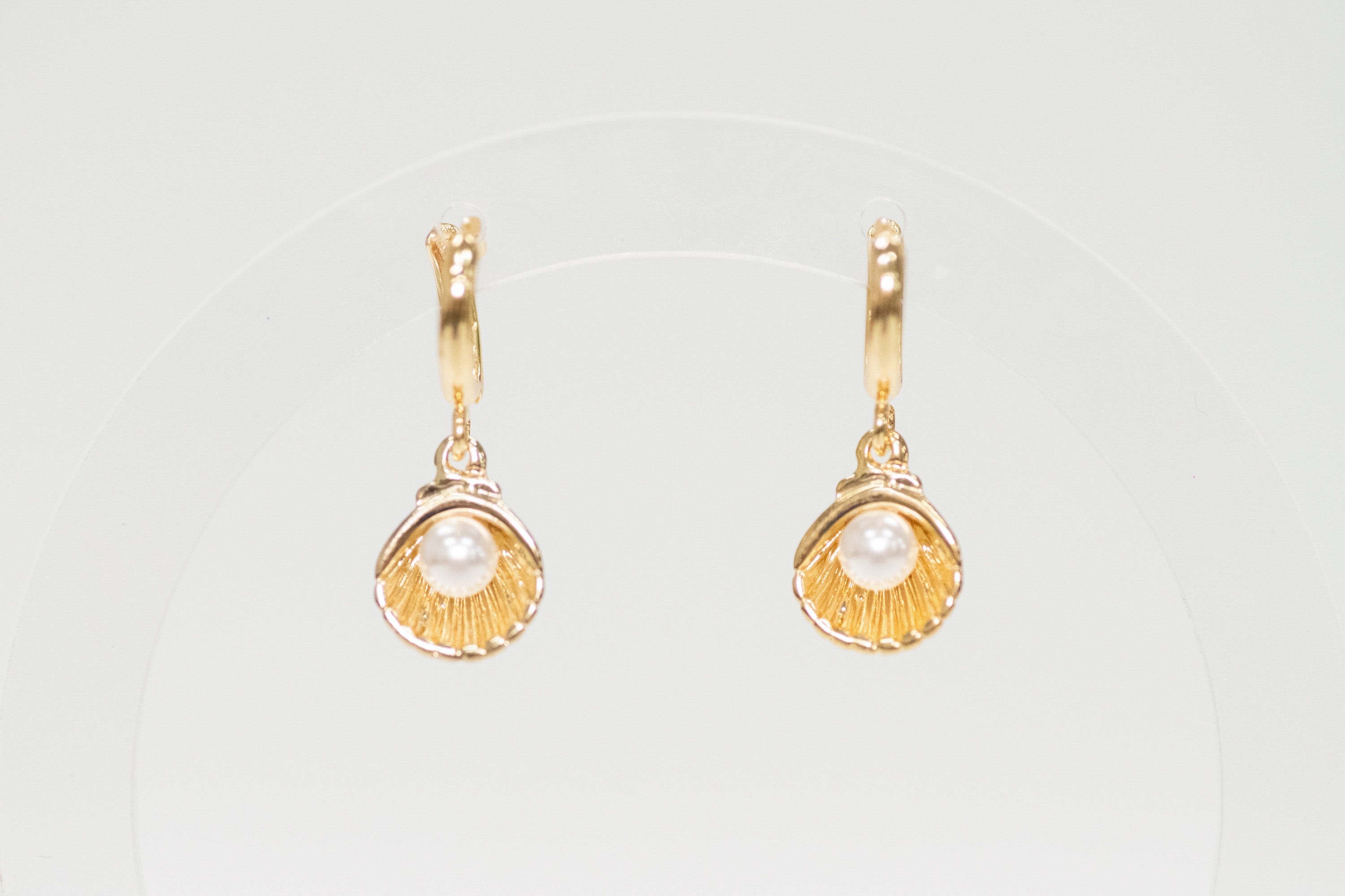 Gold shell earrings with pearl-like centers on a light gray background