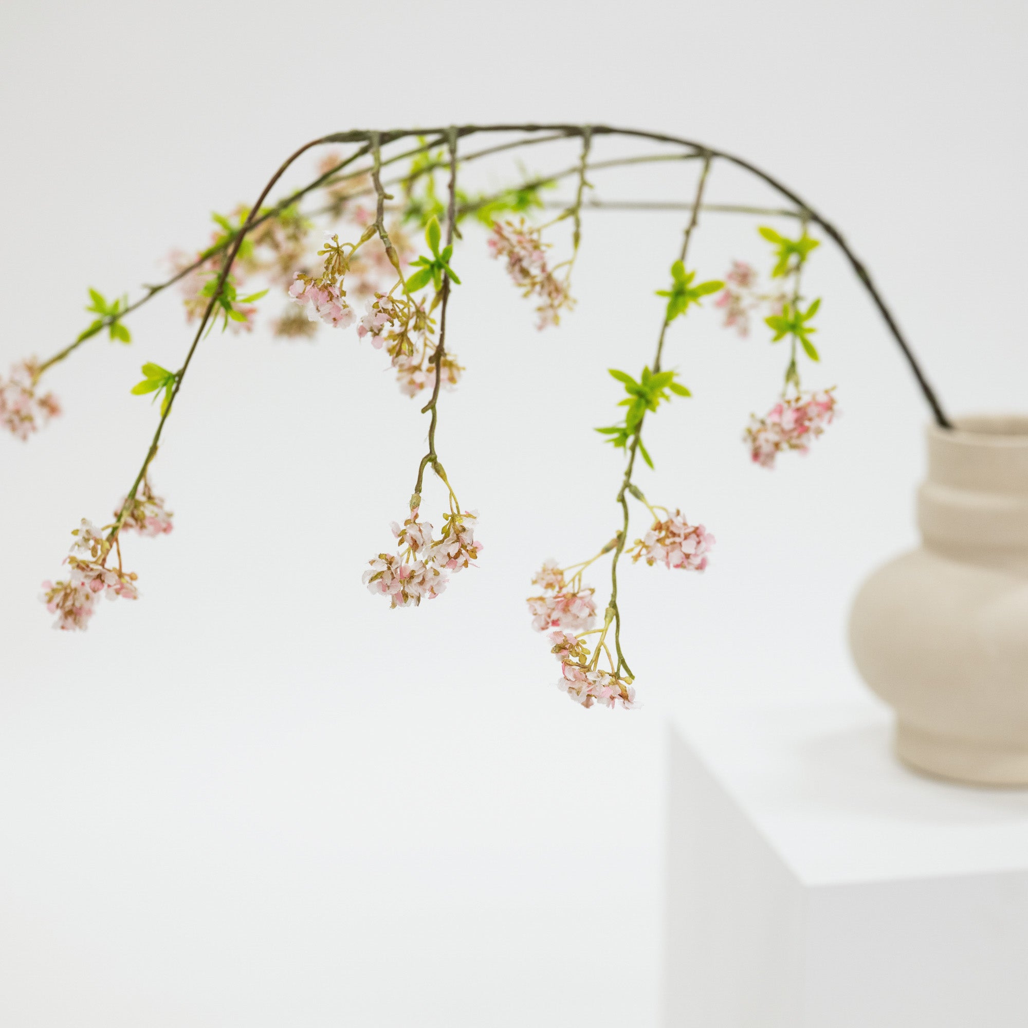 Decorative branch with pink flowers in a beige vase on a white surface