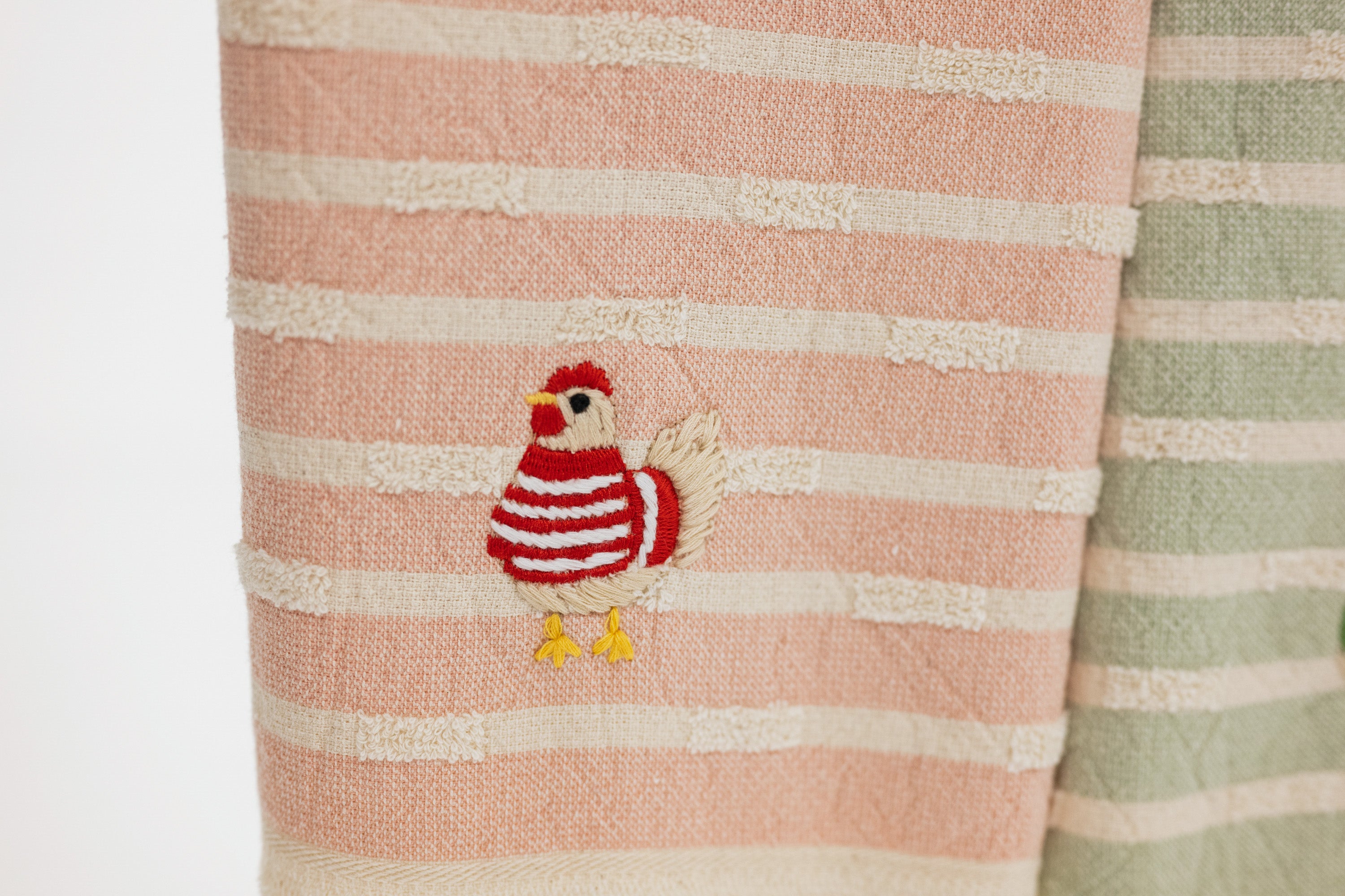 detail of embroidered chicken wearing a red and white striped sweater. on a turkish cotton striped towel