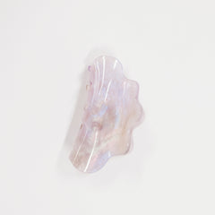 An organic-shaped resin hair claw clip with a pearlescent, iridescent finish showing soft lavender, pink, and white hues, set against a plain white background.