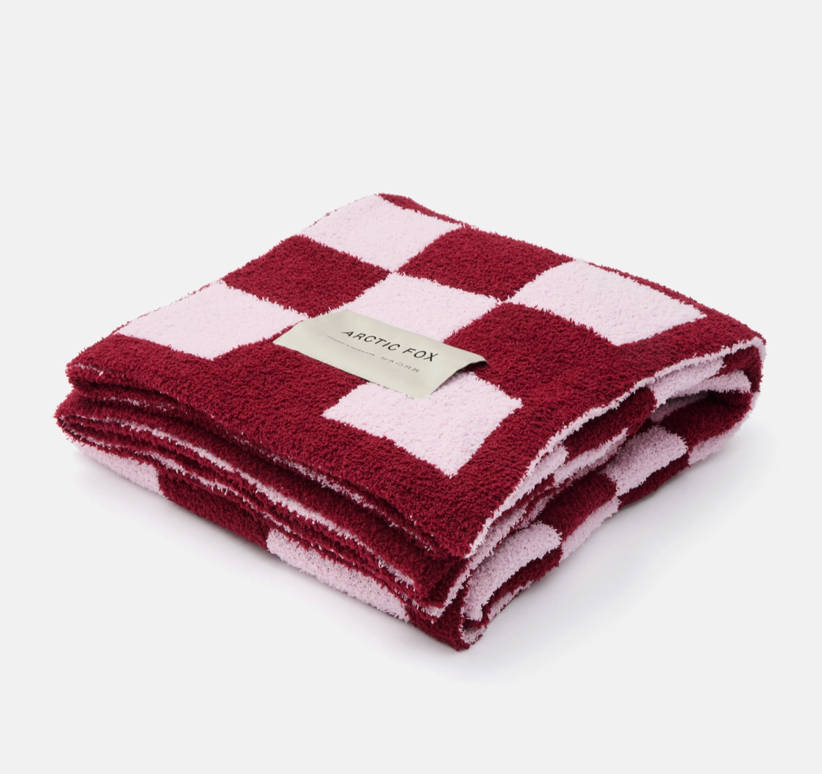 A folded plush terry cloth throw blanket featuring a pink and deep red checkerboard pattern, with a small beige paper label that reads 'ARCTIC FOX'.