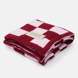 A folded plush terry cloth throw blanket featuring a pink and deep red checkerboard pattern, with a small beige paper label that reads 'ARCTIC FOX'.