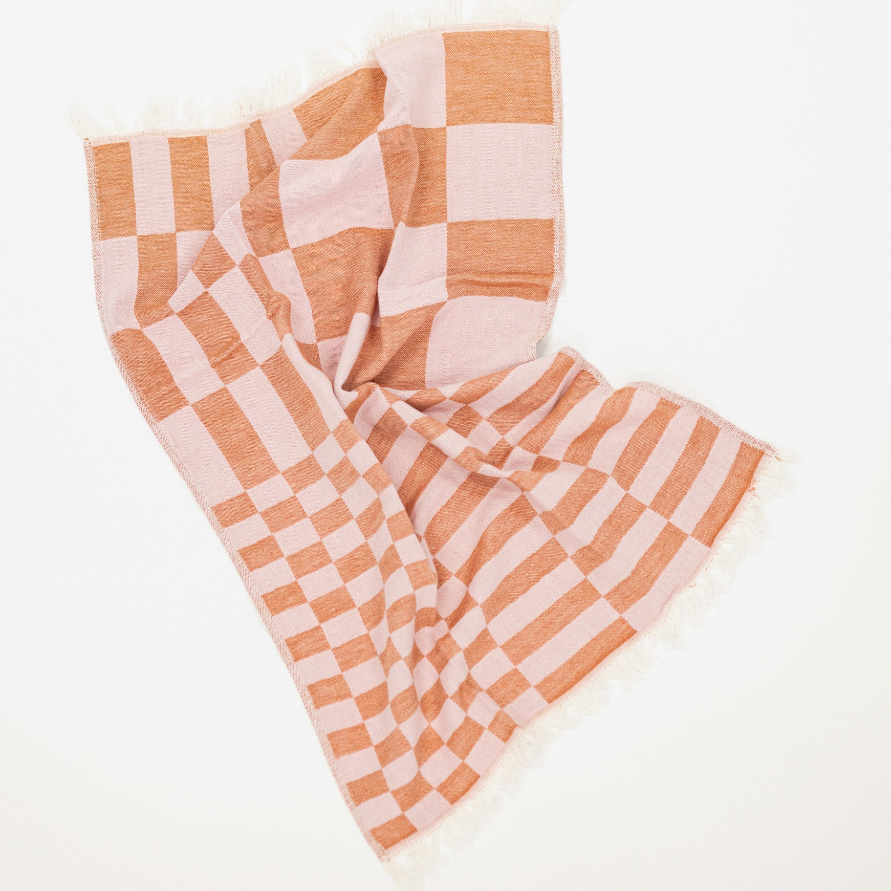 A woven kitchen towel with a light pink and deep pink checkerboard pattern and fringed edges, laid out on a clean white background.