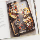Open cookbook showing a pizza on a baking tray with a scoop of tomato sauce.
