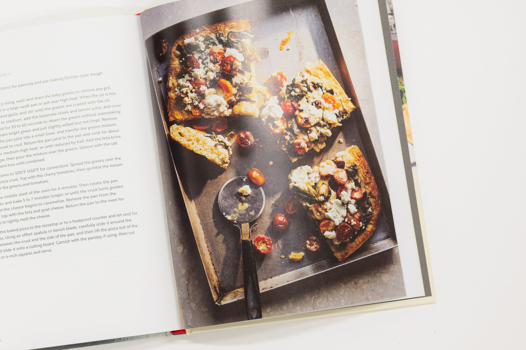 Open cookbook showing a pizza on a baking tray with a scoop of tomato sauce.