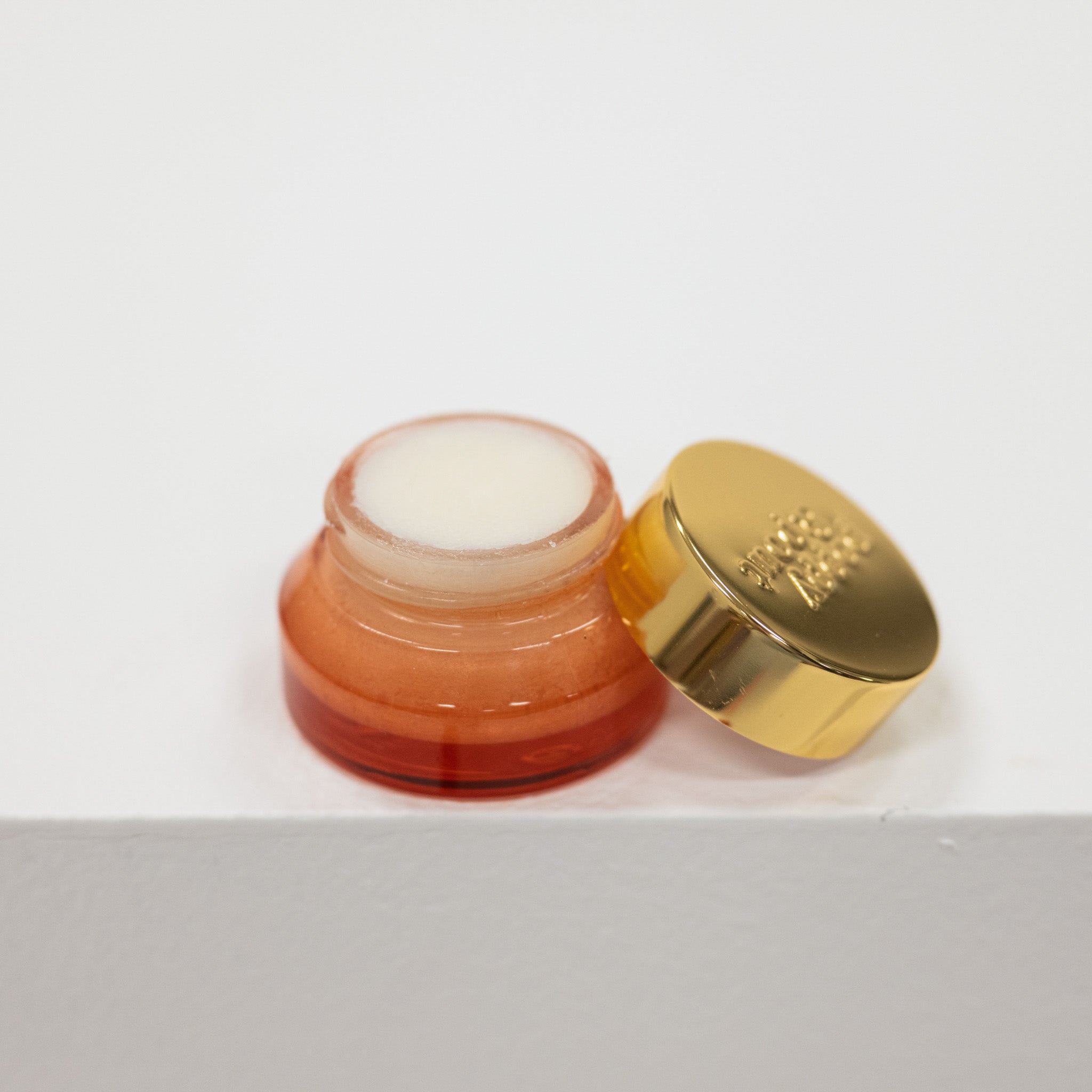 Small glass jar of lip mask with a gold lid on a white background