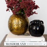 a vignette made of pressed bronze metal vase, glossy black vase, faux florals