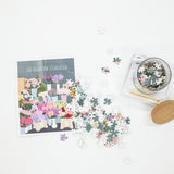 Floral-themed puzzle with pieces scattered on a white surface, accompanied by a box of additional pieces.