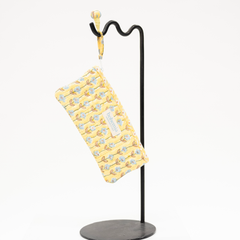 Yellow patterned pencil case bag hanging on a black stand against a white background