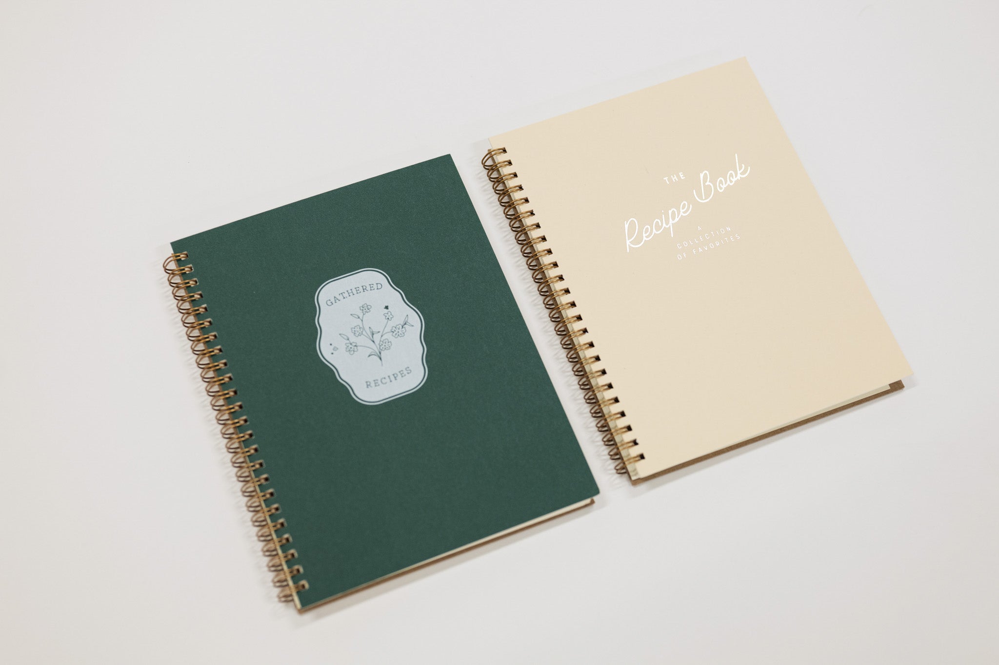 Two spiral-bound recipe notebooks, one green and one beige, on a light gray background.
