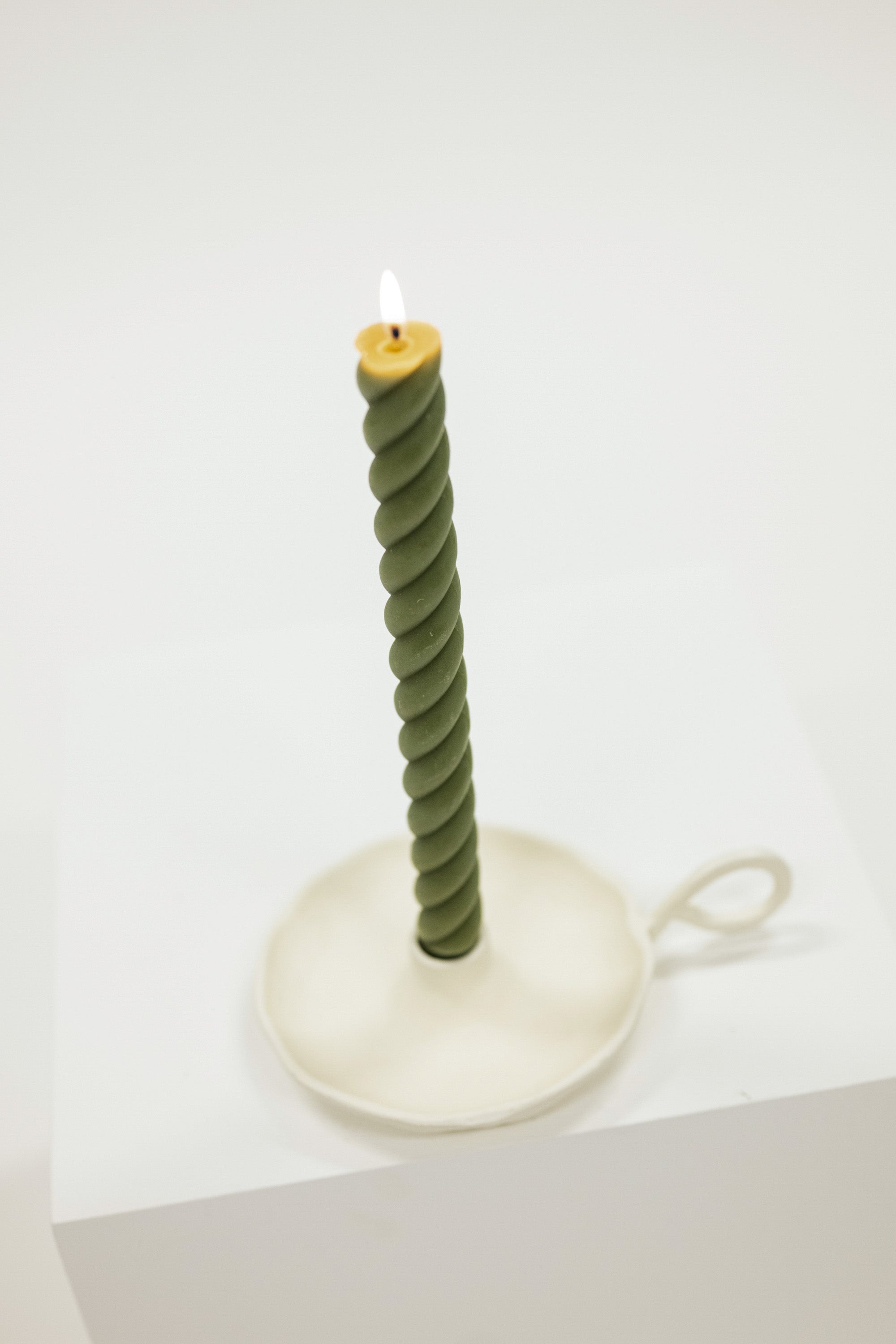 Green twisted candle on a white stand against a white background