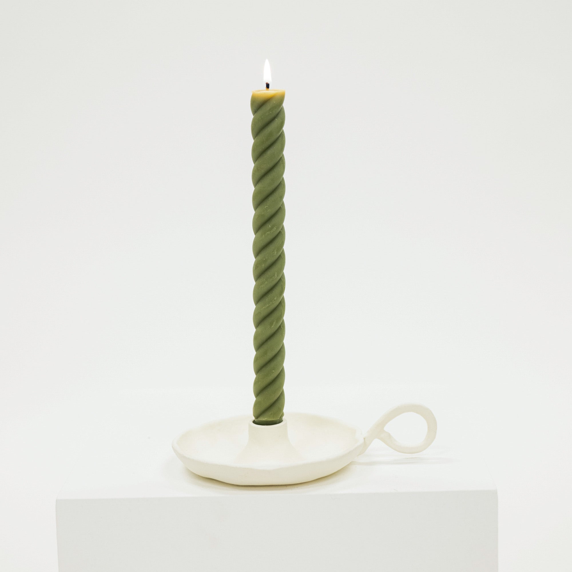 Green twisted candle on a white stand against a white background