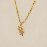 Gold necklace with a leaf-shaped pendant on a beige background
