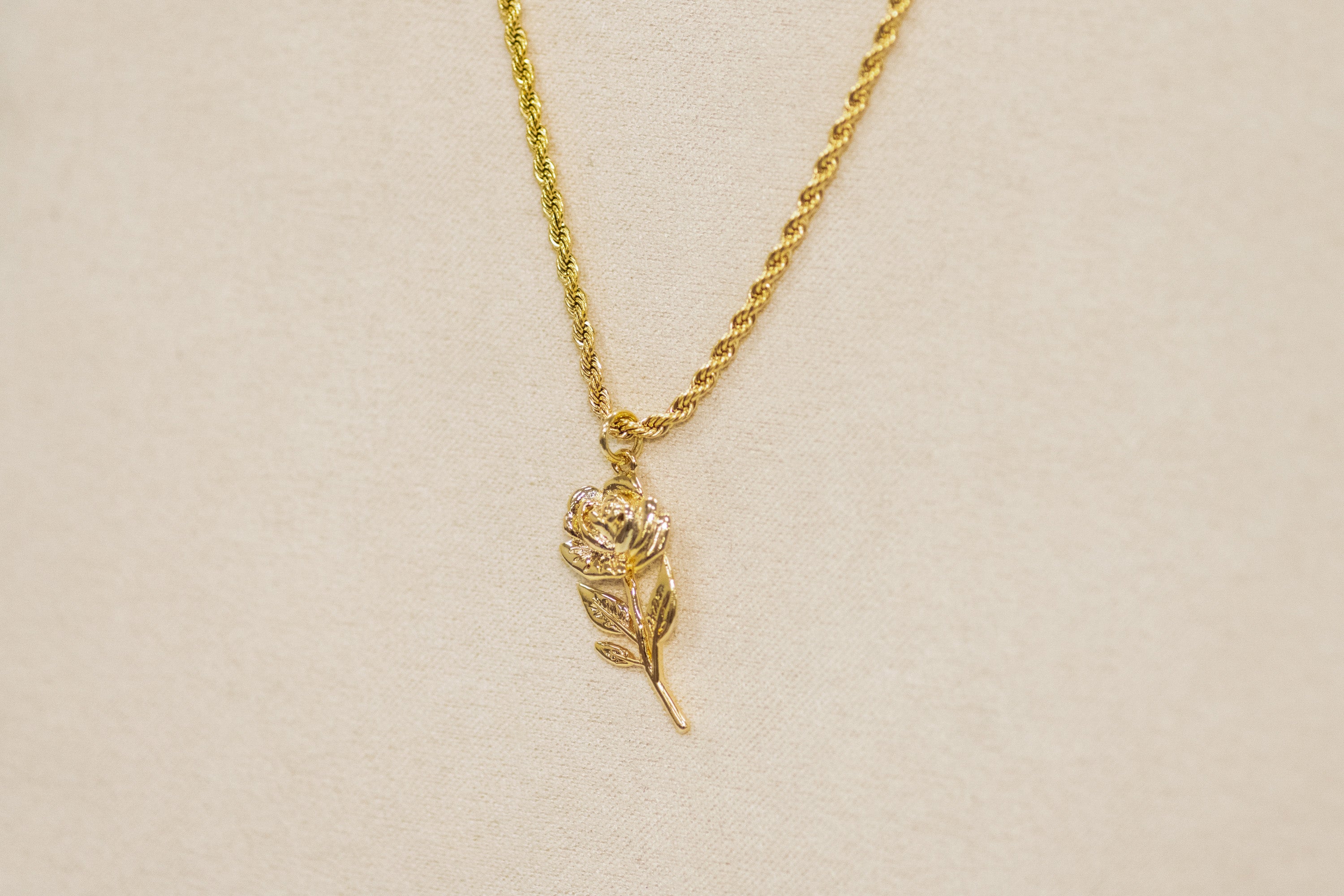 Gold necklace with a leaf-shaped pendant on a beige background