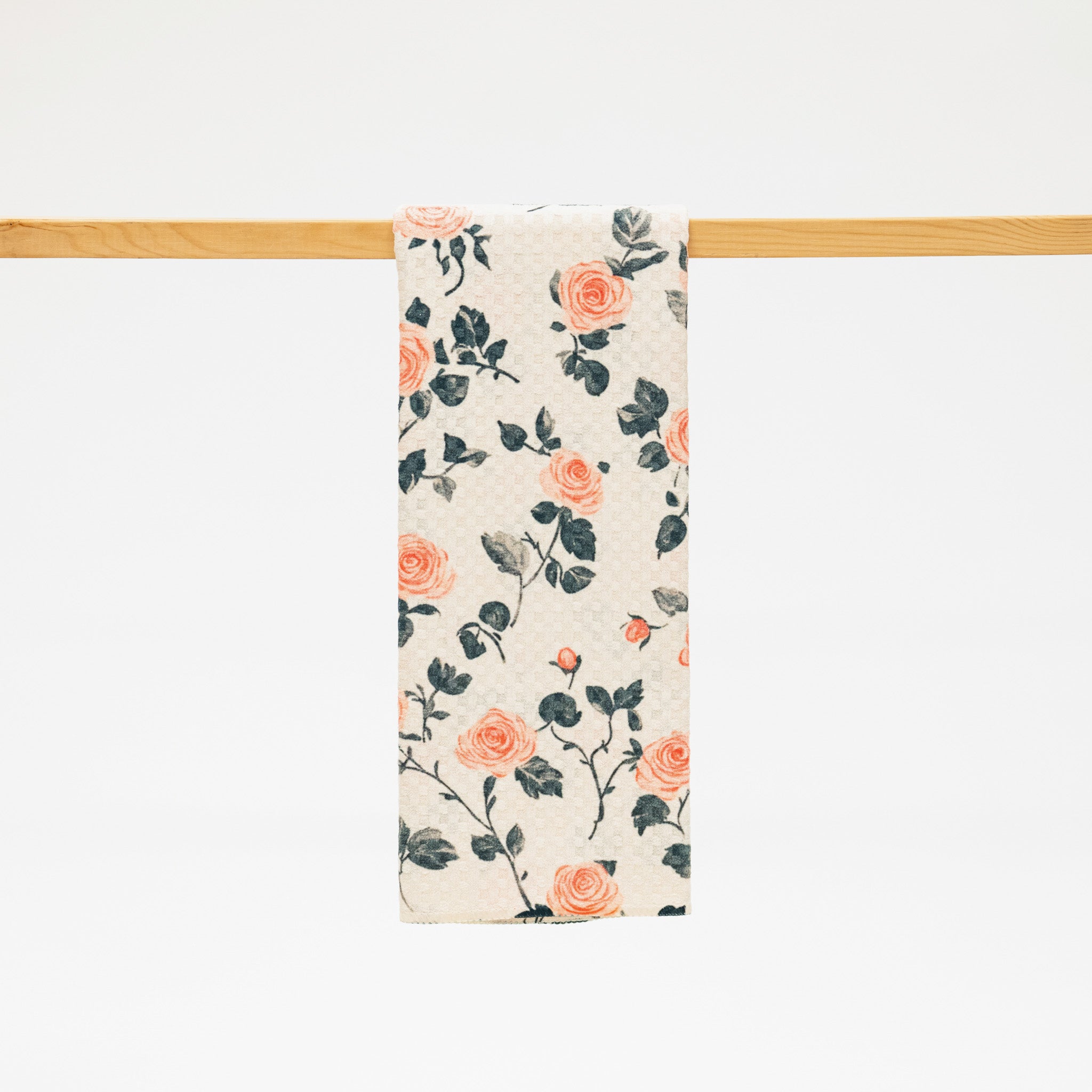 Floral patterned towel hanging on a wooden rod against a white background
