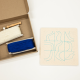 Box containing two rolls of thread next to a piece of wood with a design on a white background