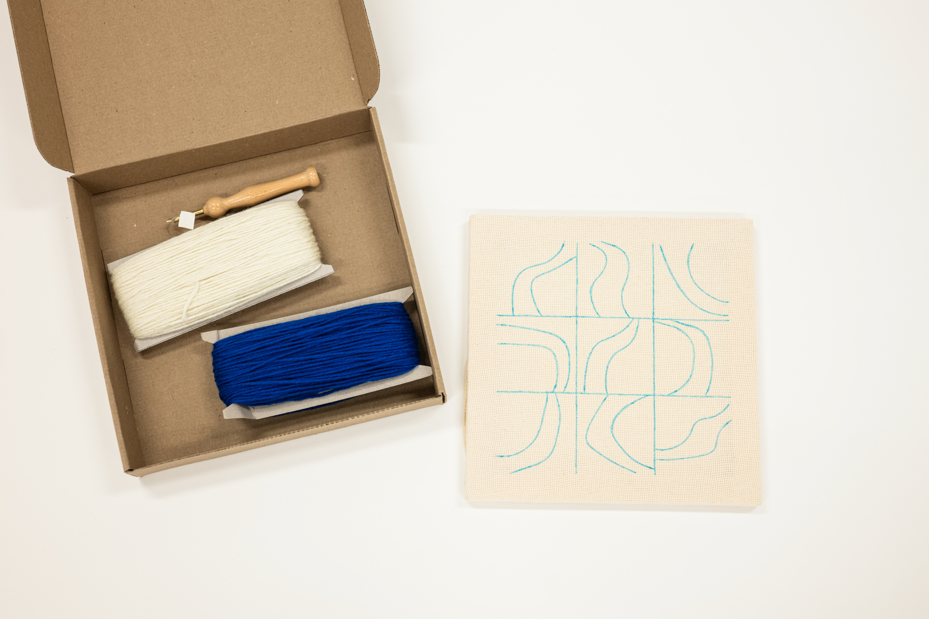 Box containing two rolls of thread next to a piece of wood with a design on a white background