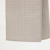 A close-up of a light beige woven fabric with a subtle geometric pattern, hanging against a plain white background.