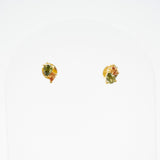 A pair of small gold stud earrings with green and orange stones, displayed on a white arched jewelry stand.