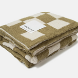 A folded fleece throw blanket with a checkered pattern in olive green and cream, featuring a white paper label that reads 'ARCTIC FOX'.