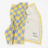 A woven kitchen towel with a yellow and blue checkered pattern on one side and a cream-colored center with a yellow border and small fish embroidery, displayed on a white background.
