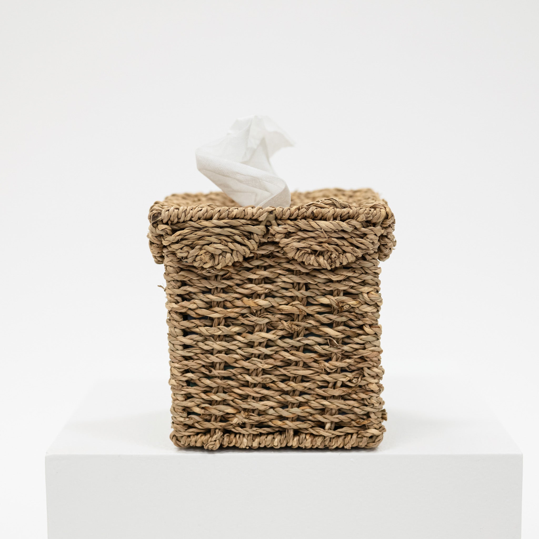 Woven tissue box cover with tissues on a white background