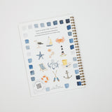 A spiral-bound watercolor painting guide book titled 'Learn to paint with watercolor' by Julia Lee, featuring a nautical theme with illustrations of a sailboat, crab, lighthouse, starfish, octopus, anchor, and striped beach chair, displayed on a light gray background.