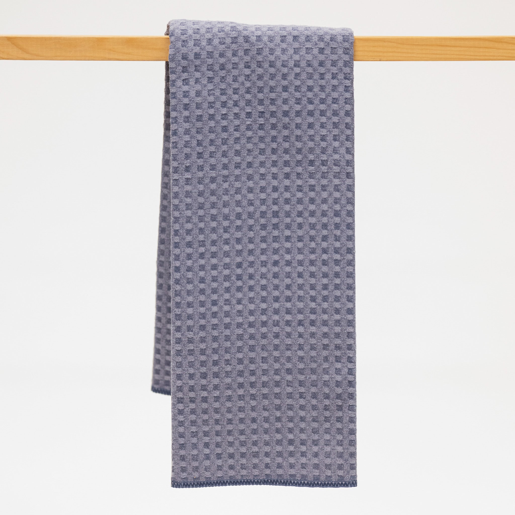 Gray blue textured towel hanging on a wooden rod against a white background