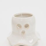 A white ceramic ghost-shaped candle holder with cutout eyes and mouth, shown on a plain white background with a candle inside.
