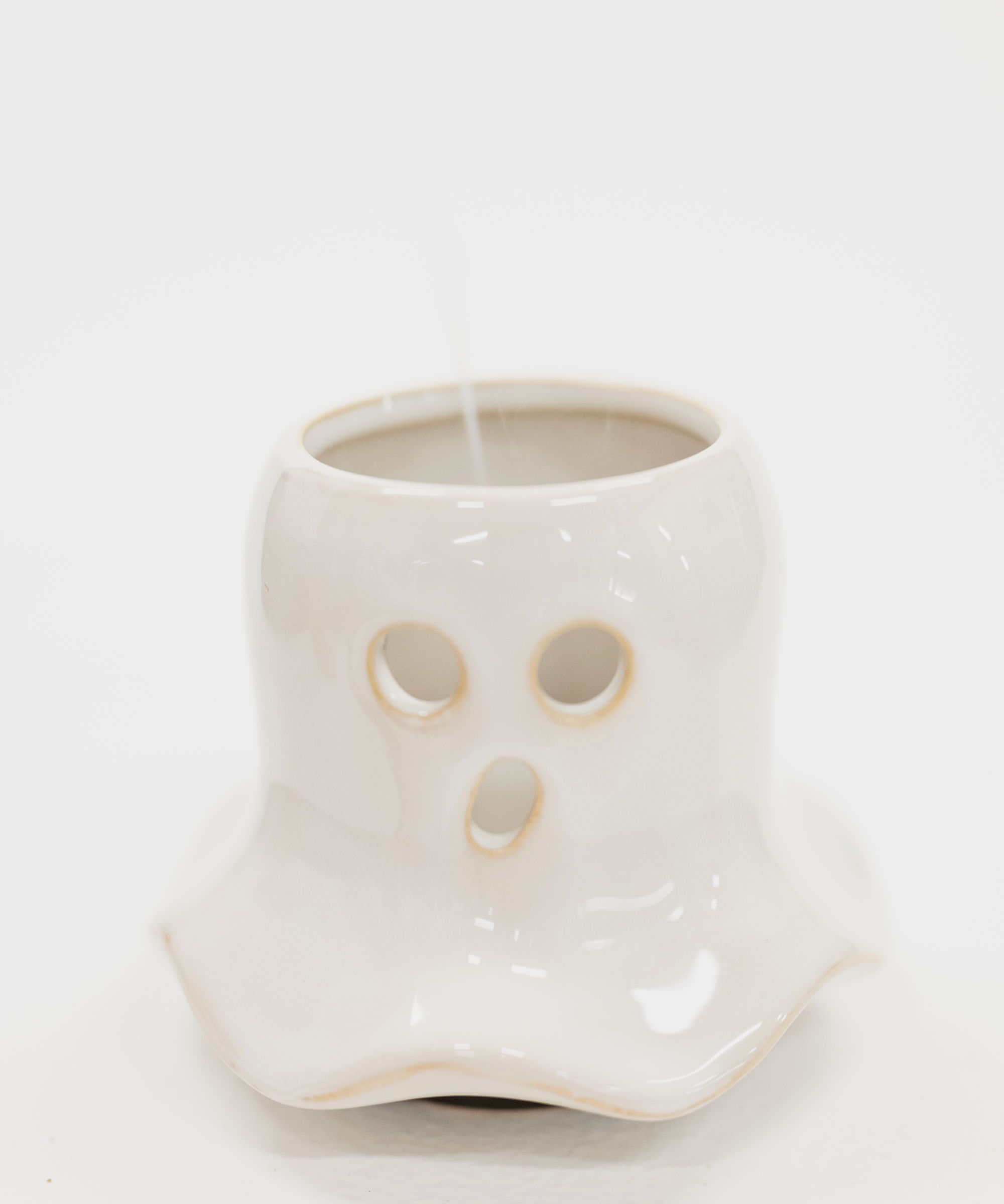 A white ceramic ghost-shaped candle holder with cutout eyes and mouth, shown on a plain white background with a candle inside.