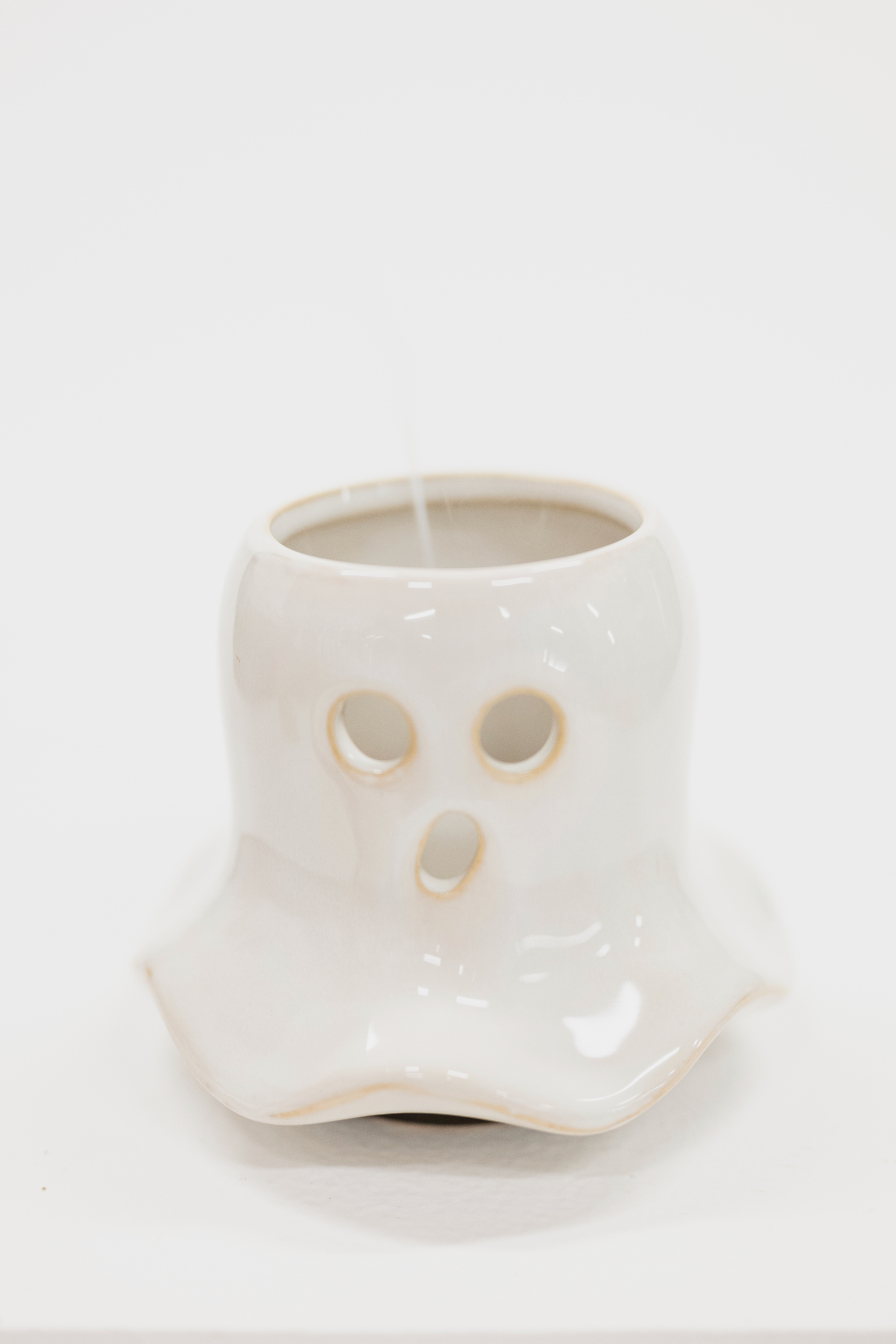 A white ceramic ghost-shaped candle holder with cutout eyes and mouth, shown on a plain white background with a candle inside.