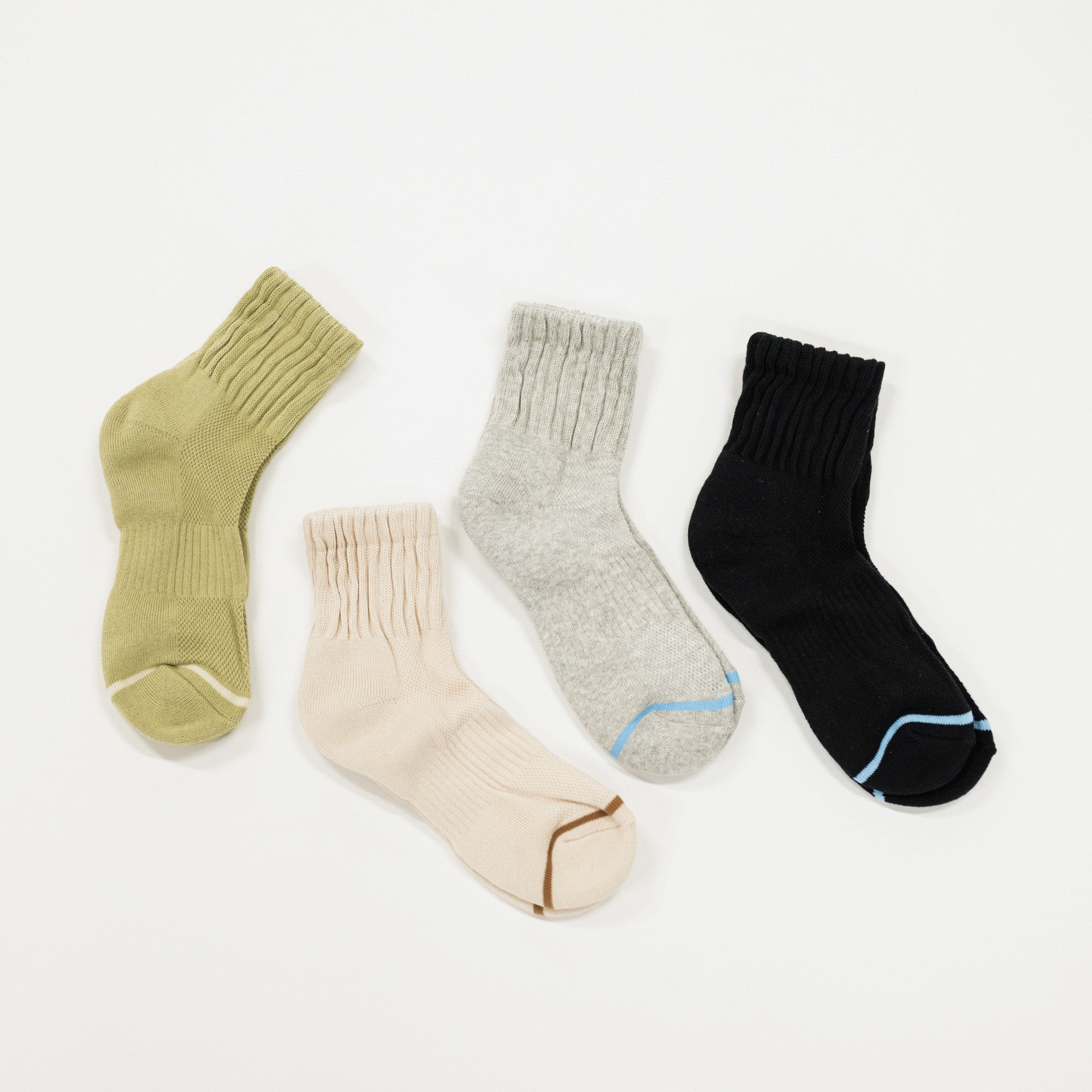 Four ribbed ankle socks laid flat on a white background: one olive green, one cream, one heather gray, and one black, each with a contrasting accent line near the toe.