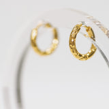 Gold hoop earrings on a clear stand with a white background