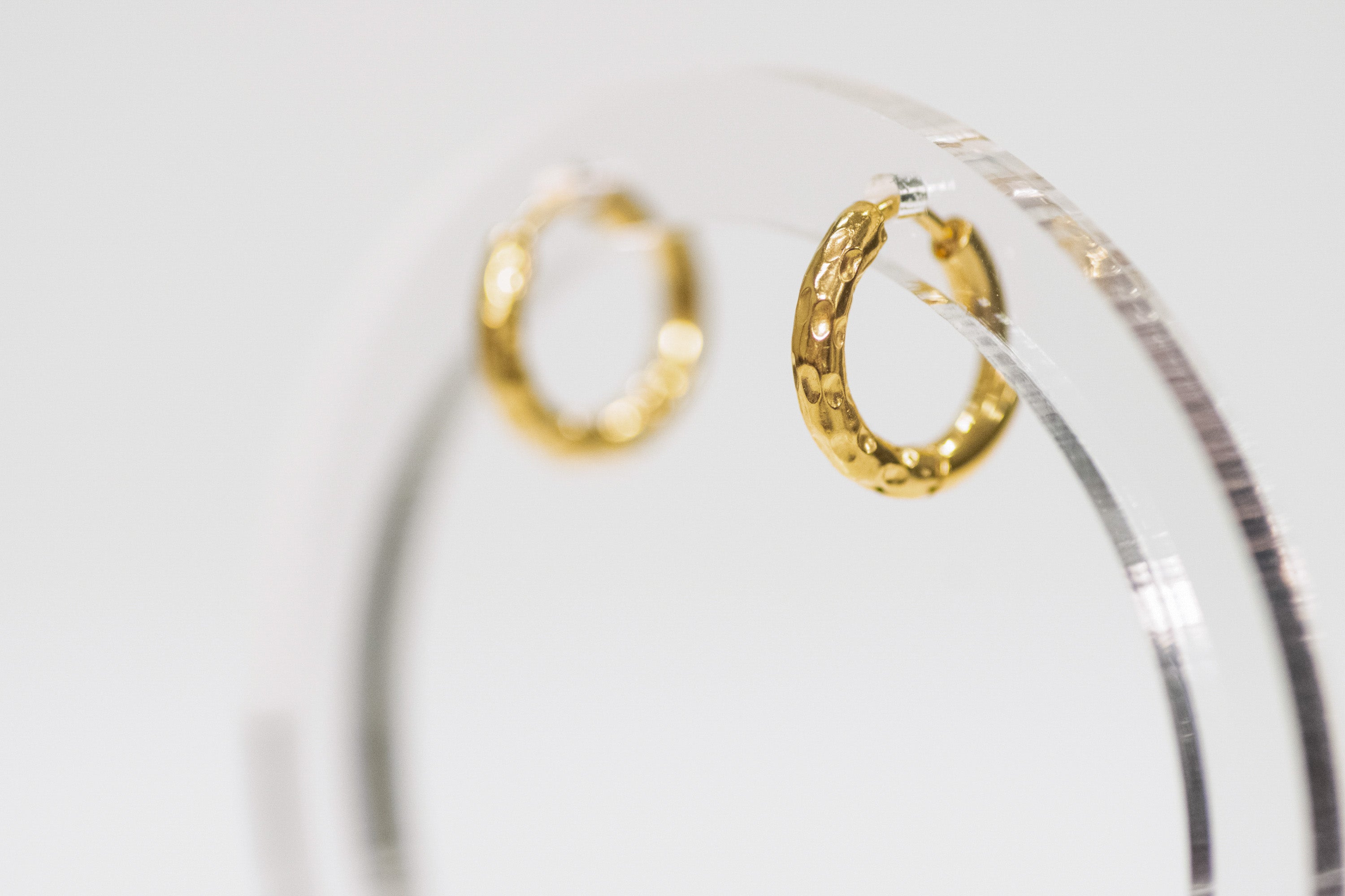 Gold hoop earrings on a clear stand with a white background