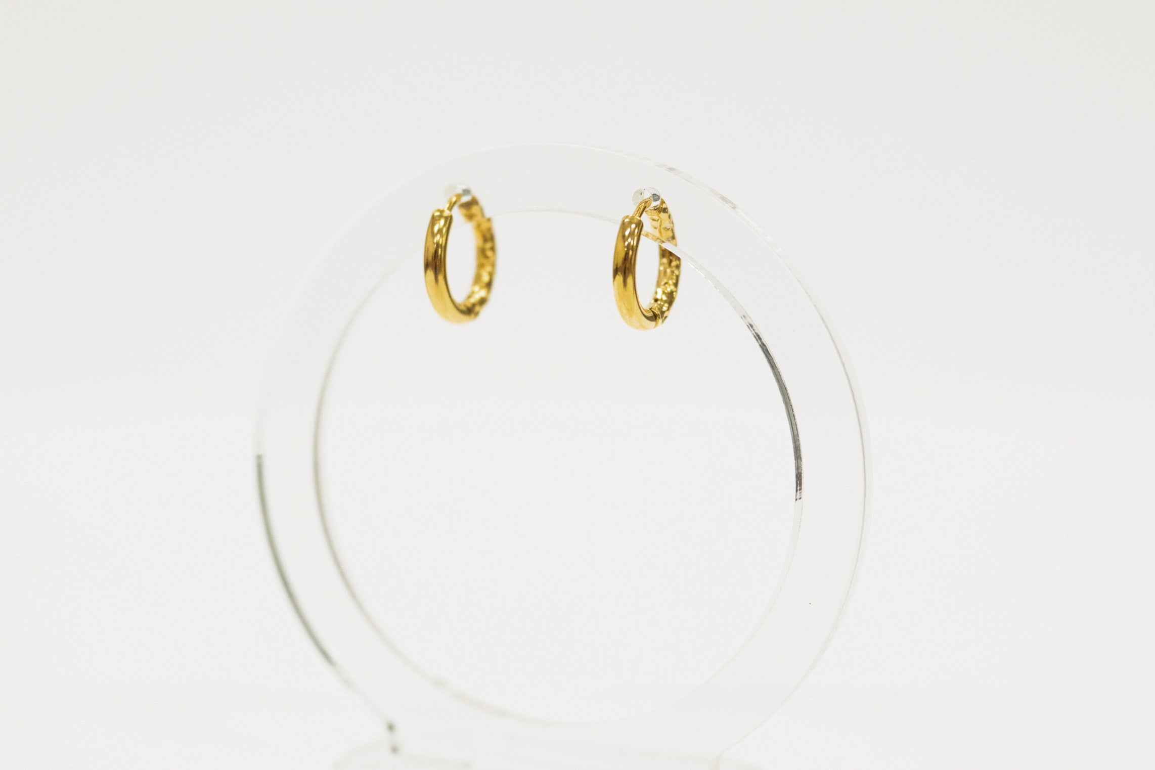 Gold hoop earrings on a clear stand against a white background