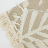 Beige and white patterned beach towel with tassels on a light background