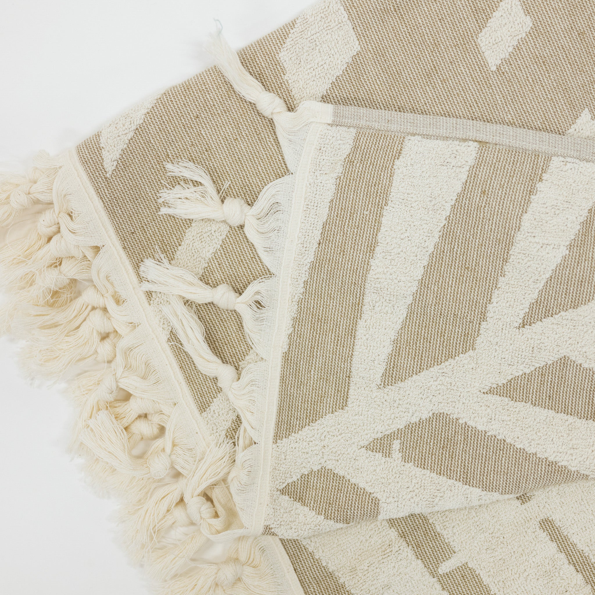Beige and white patterned beach towel with tassels on a light background